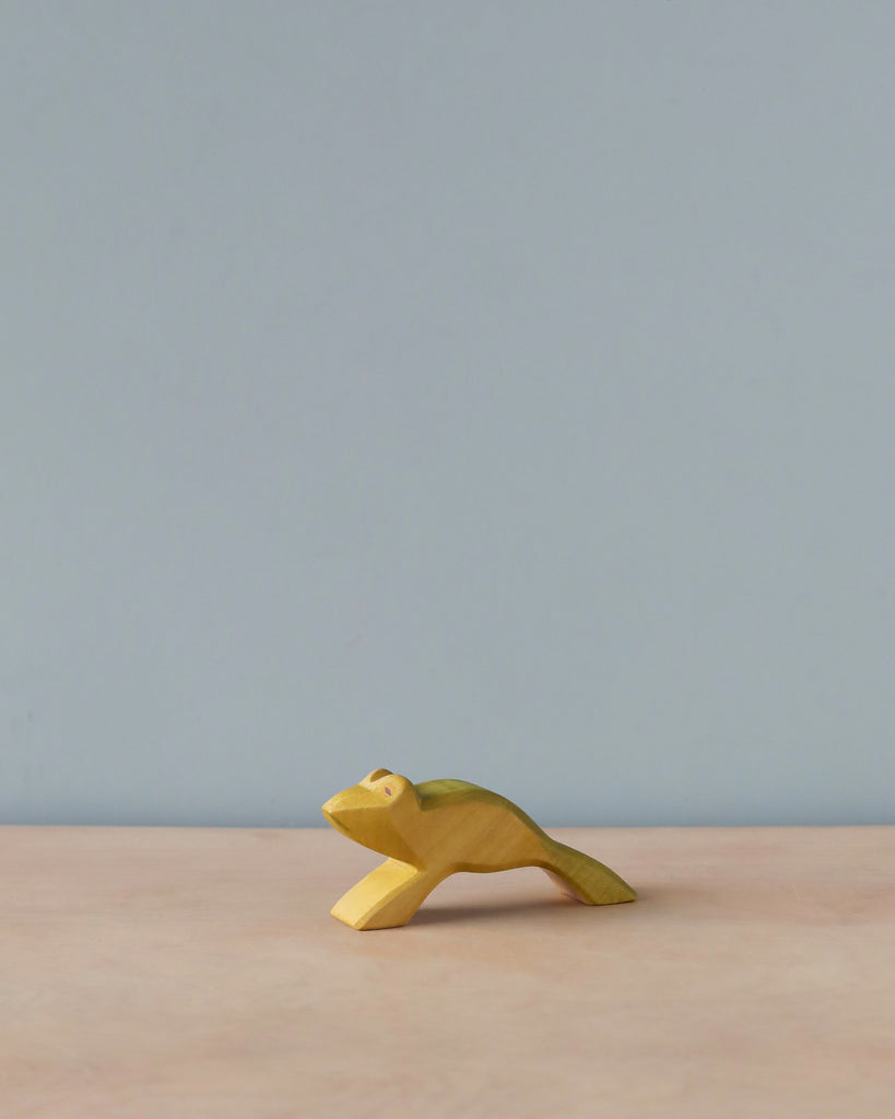 A Handmade Holzwald Jumping Frog, painted yellow, positioned on a flat surface against a plain light grey background, from the Holzwald Brand.