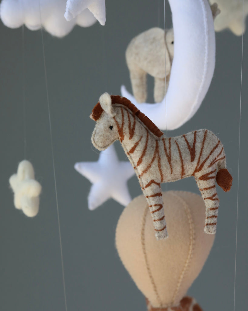 A close-up image of a Handmade Mobile - Day Dreamer - Final Sale featuring a striped zebra, hearts, and stars in soft neutral tones hanging against a blurred gray background.