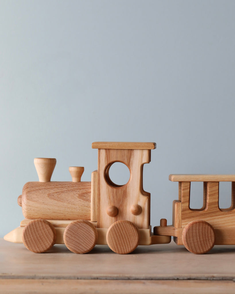 A handmade Handmade Wooden Train - Extra Long set consisting of an engine and two cars, featuring smooth, natural beech wood tones against a soft blue background.