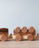 A Handmade Wooden Train - Extra Long with cylindrical carriages featuring circular wheels, displayed against a muted blue background.