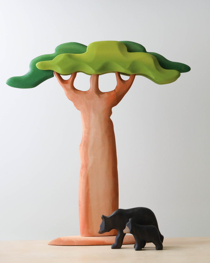 A small sculpture of an Extra Large Wooden Tree with a wavy green canopy and a smooth, beige trunk made from linden wood, next to a smaller black bear figure, against a plain white background.