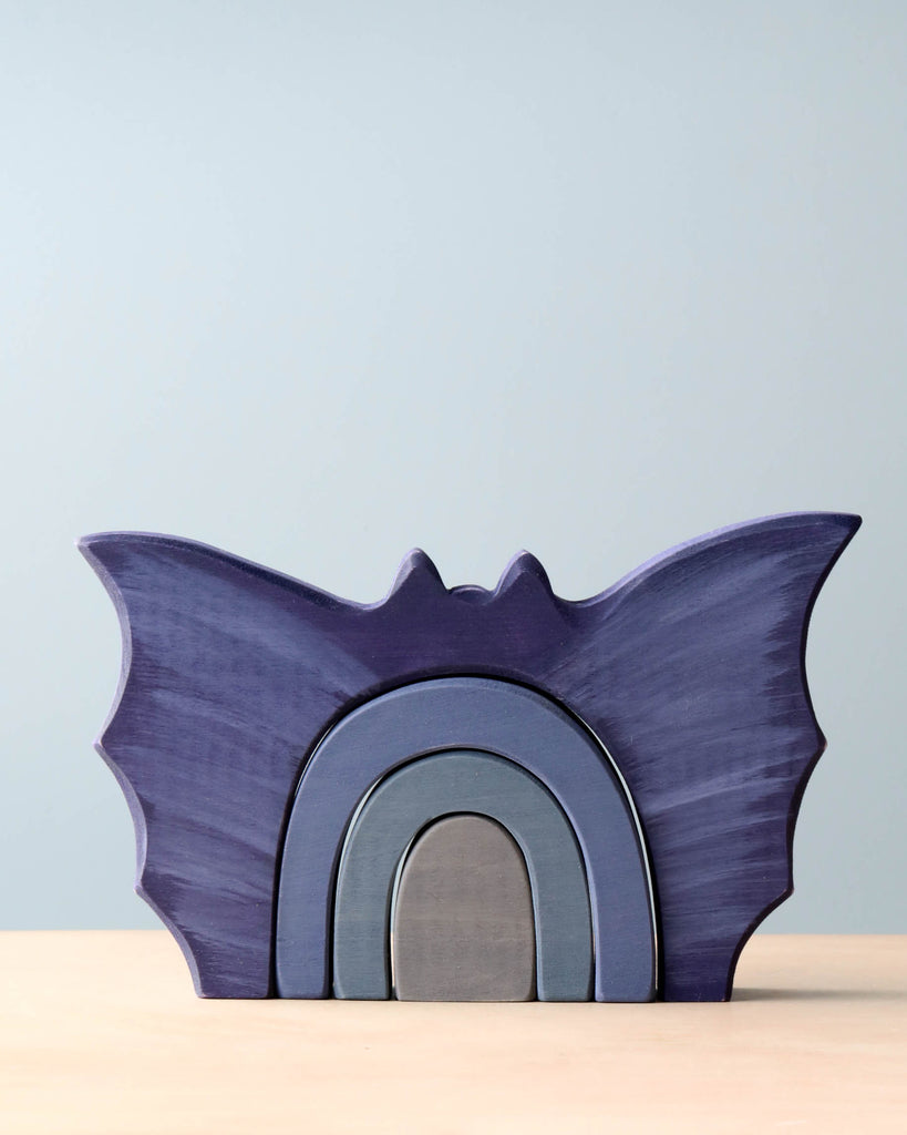 A Handmade Wooden Bat Stacker in shades of purple and gray, crafted from poplar hardwood, featuring a simple design with layered arches, displayed against a soft blue background.