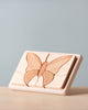 A Handmade Wooden Puzzle with a butterfly design, made from rich Cherry wood. The puzzle pieces showcase different shades of natural wood, fitting elegantly into a rectangular frame. Handmade in Russia and finished with linseed oil, the background is plain and light gray.