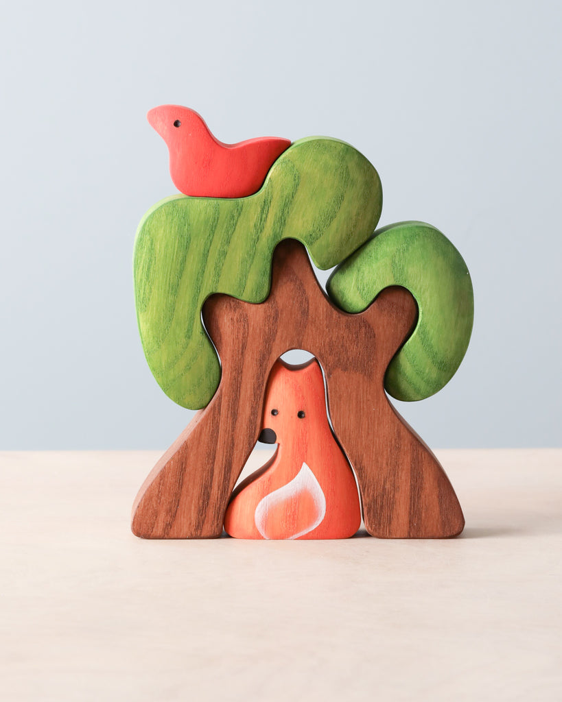 A Handmade Wooden Tree with Fox featuring two trees with green canopies, a red bird perched on top, and a small, orange flame-like figure nestled between the tree trunks. The interlocking pieces are designed in playful, rounded shapes and finished with food grade flaxseed oil for a safe and natural touch.