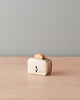 A vintage cream-colored Maileg | Miniature Toaster with a single orange slice of toasted bread on top, sitting on a wooden surface against a plain light blue background.