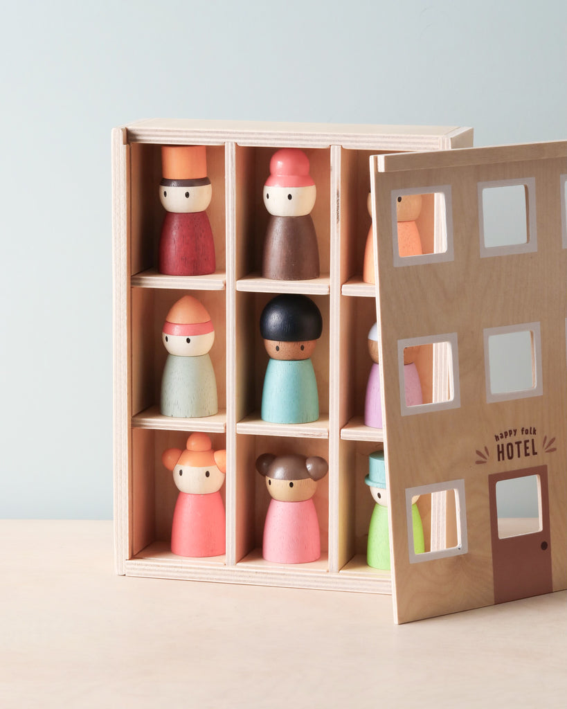 Wooden toy featuring a box labeled "Happy Folk Hotel" with an open lid showing a grid of nine compartments, each holding a colorful wooden peg doll resembling people in different attire. Crafted from solid wood, the design exudes a playful and minimalistic aesthetic, perfect for creative play.