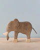 A handcrafted Holztiger Elephant stands on a light wooden surface against a pale blue background. The elephant has a simple, minimalist design with light and dark brown tones. Like other HOLZTIGER figures, it’s made in Europe, ensuring quality and craftsmanship.