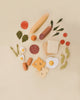 Assorted Sabo Concept Handmade Wooden Breakfast Set items including fruits, vegetables, bread, cheese, and meats arranged creatively on a beige background.