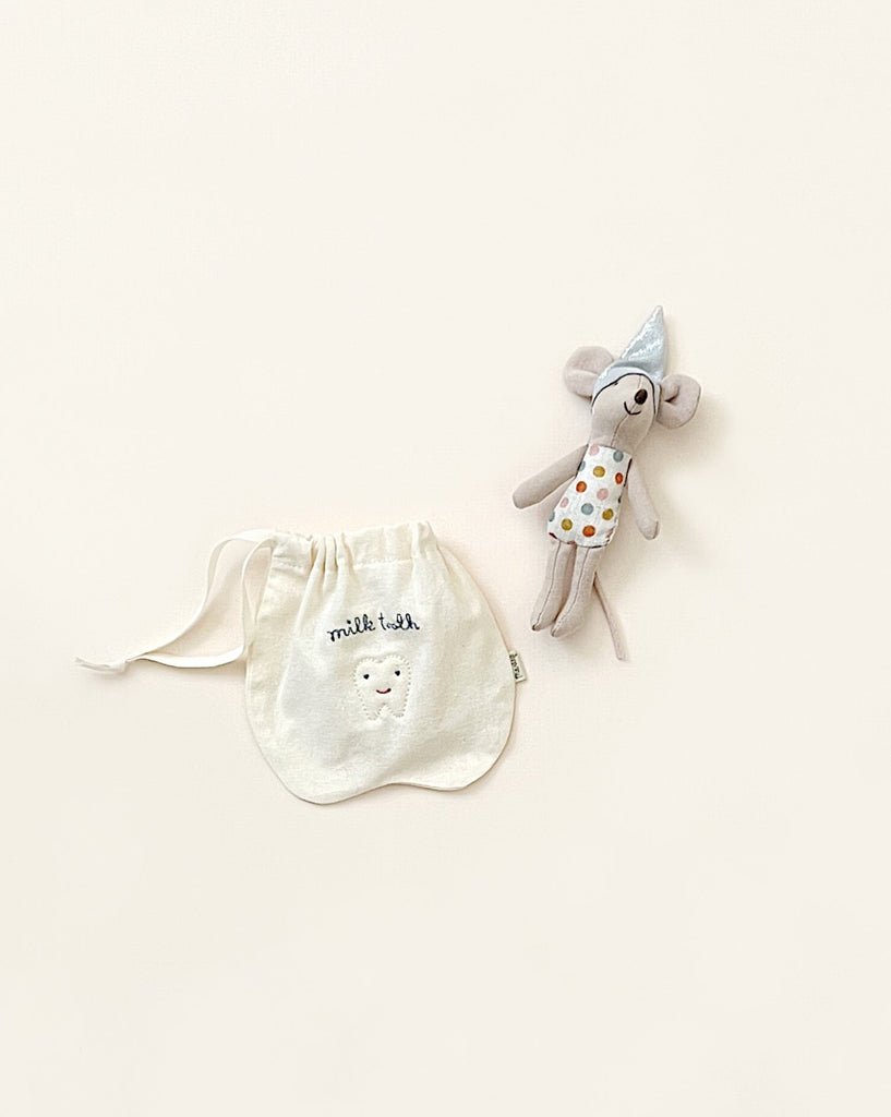 A small fabric pouch with a smiling cloud and the text "milk tea" printed on it is placed next to a gray plush toy mouse wearing a colorful polka-dotted outfit and a party hat. This cute little bag makes the perfect Maileg Tooth Fairy Little Mouse gift for those baby teeth. The background is a soft off-white color.