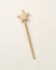 A Handmade Wooden Magic Wand, carved from beech wood, lies flat on a light beige surface. The wand features a simple design with a straight handle and a star-shaped top, showcasing its natural light-colored wood.