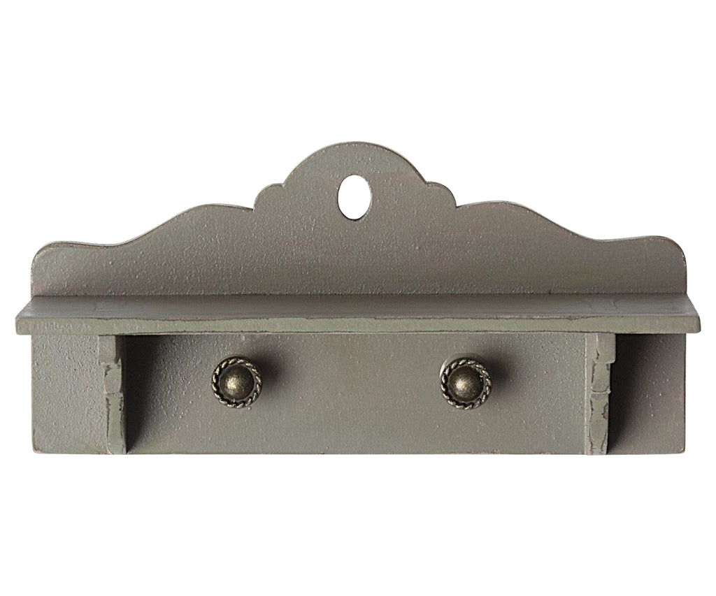 A small, decorative gray Maileg Miniature Dollhouse Shelf with a scalloped top edge perfect for Maileg Dollhouse decor. It features two metal hooks with round decorative bases on its lower front side and a hole in the top center for wall mounting. The shelf has a rustic, vintage appearance.