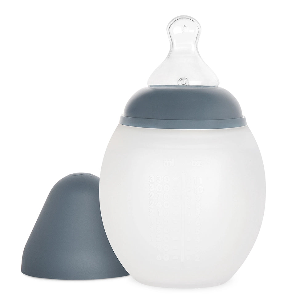 A Medical Grade Silicone Baby Bottle with a grey cap and silicone nipple, featuring measurement markings on its frosted translucent body. The bottle is displayed with its matching grey base detached.