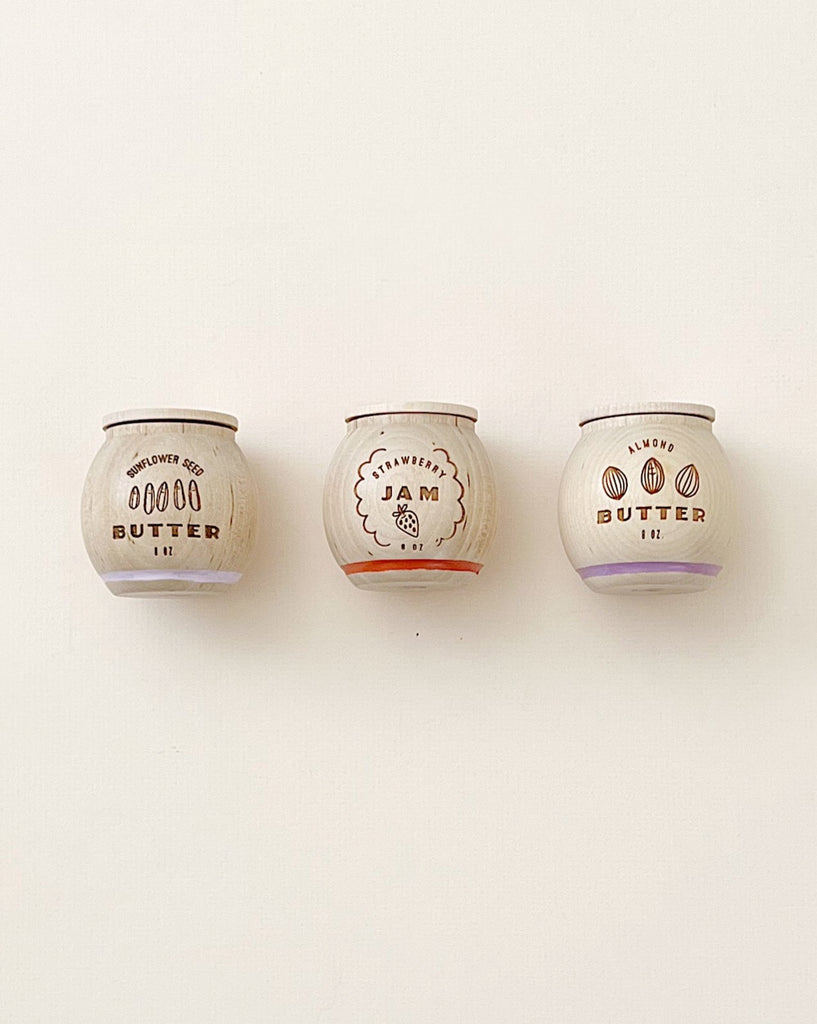 Three small jars of Milton & Goose Jam & Nut Butter Pretend Play Food flavored with almond butter, strawberry jam, and cinnamon, labeled respectively, neatly displayed against a plain white background.