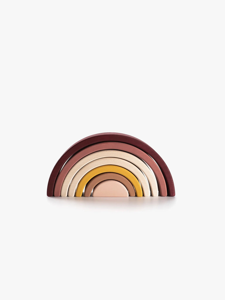 The Handmade Rainbow Stacker - Pink is a minimalist wooden rainbow comprised of seven arcs in muted shades of brown, beige, yellow, and pink. Ideal for open-ended play, each arc nestles inside the other and is coated with non-toxic paint. Displayed against a plain white background, it ensures both safety and aesthetic appeal.