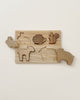 A Handmade Wooden Woodland Puzzle featuring simple, animal-shaped pieces, including a rabbit, snail, squirrel, sheep, bear, and elephant. Each piece fits into corresponding slots on a rectangular wooden board coated with linseed oil and beeswax. One piece, shaped like a rabbit, is slightly lifted from its slot.