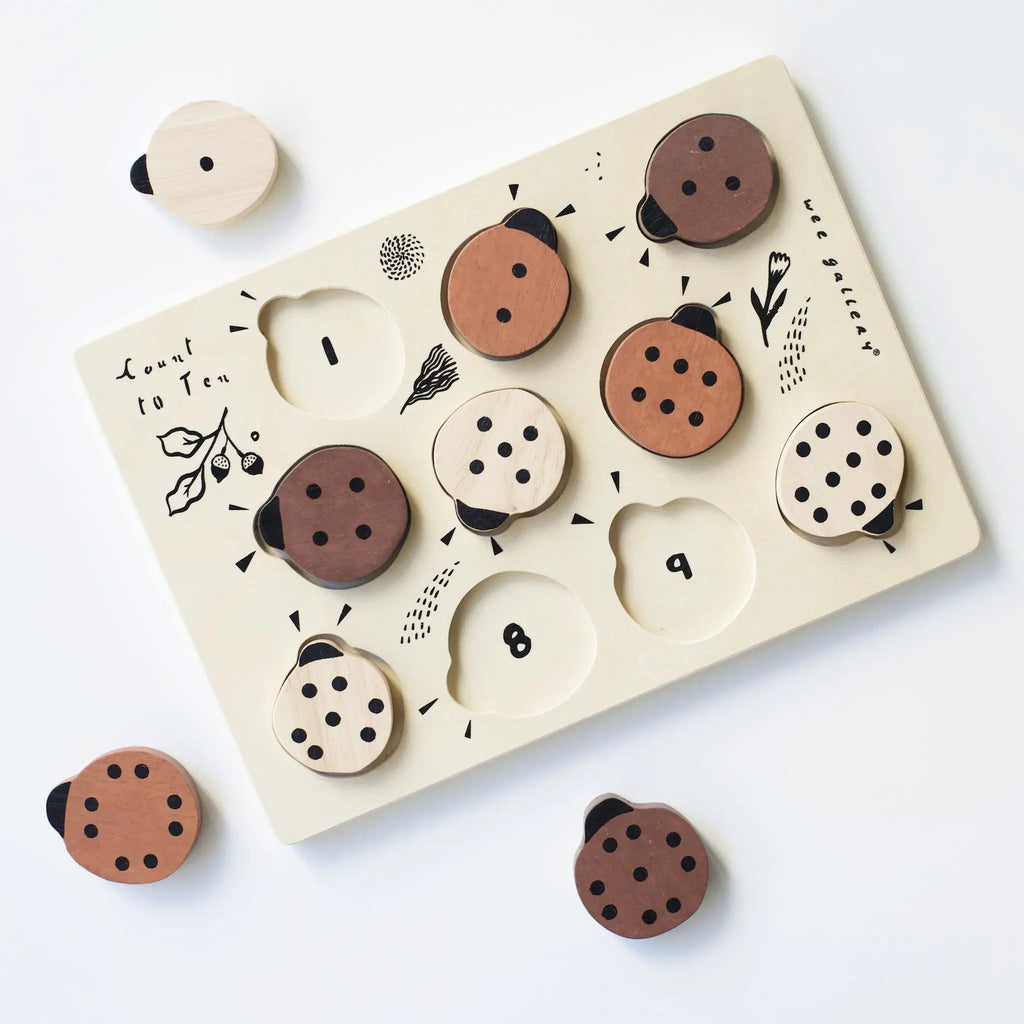 Wooden Tray Puzzle - Count to 10 Ladybugs with various abstract face designs on circular pieces, set against a white background. Each piece fits into corresponding slots on a cream-colored board made from sustainably sourced rubberwood.