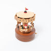 A Christmas Carousel Music Box shaped like a carousel with carved details, designed for ages 12 and up. It features small figurines of a clown and various animals, including elephants. The base is ornately decorated, crafted from sustainably sourced wood, and includes a crank for winding the music.