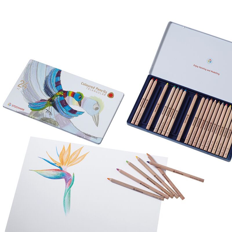 Open box of Stockmar Colored Pencils Triangular Assortment 24+1 with a case set next to an illustration of a colorful bird and a flower on white paper, showcasing art supplies and creativity.