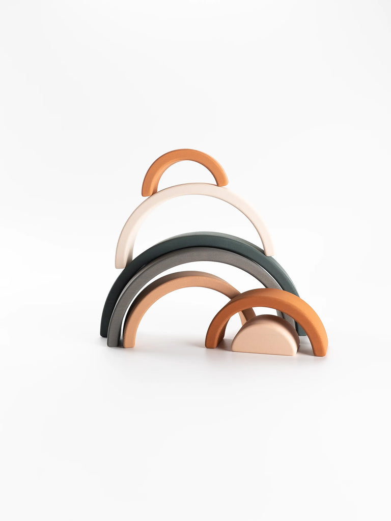 Introducing the Handmade Rainbow Stacker - Mojave Desert, a stacking toy set featuring five elegantly curved, minimalist pieces in shades of white, green, and terracotta. Crafted by hand with non-toxic paint, the arches gracefully decrease in size from back to front, offering a visually appealing and modern design against a plain white background.