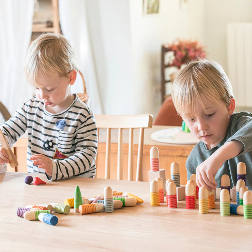 Two young children, focused and engaged, playing with colorful wooden Grapat Buds/Brots on a table in a brightly lit room.