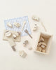 A collection of Hinoki wood toy kitchen utensils and Velcro Wooden Vegetables neatly arranged next to a small wooden crate and a blue and white checkered cloth on a light background.