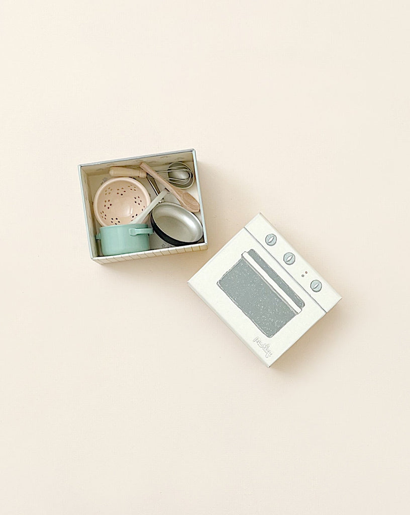 A Maileg Cooking Set including a pot, utensils, and a playful stove box, all displayed against a pastel background.