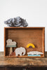 A **Wooden Safari Set** featuring hand-painted Maple wood animals includes a lion on a tree, an elephant, and a crocodile. A piece of crumpled gray paper resembles a cloud above the scene, with a two-part semi-circular yellow and brown sun element adding detail, promoting fine motor skills development.