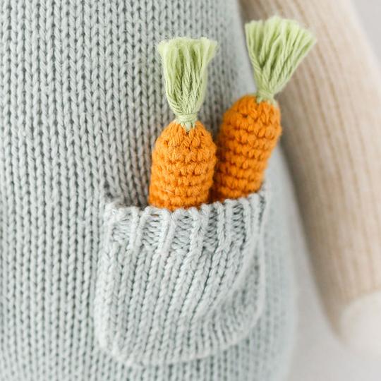 Two Cuddle + Kind Bunny toys with green tassels, filled with hypoallergenic polyfill, poking out of a cozy gray sweater pocket.