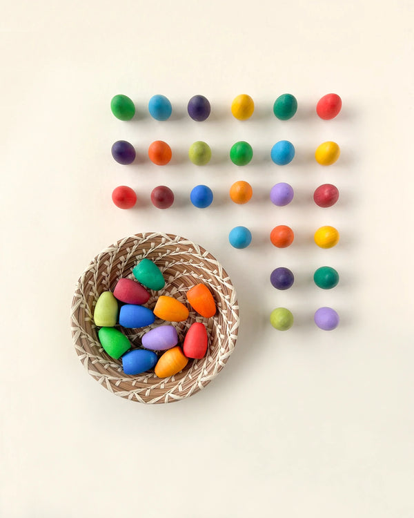 A basket of Grapat Mandala Rainbow Eggs, positioned next to neat rows of multicolored balls arranged in a grid on a light background.