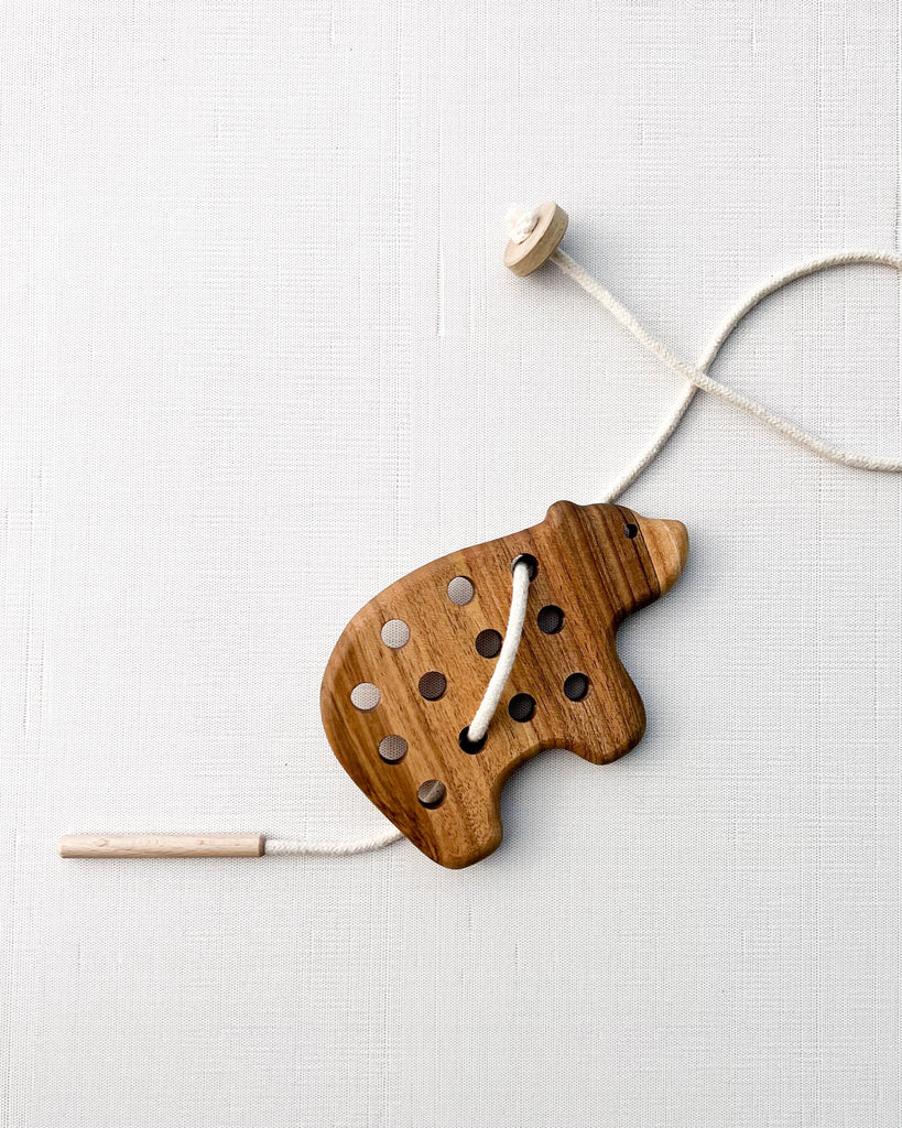 Handmade Bear Lacing Toy designed for developing hand-eye coordination, with holes and a string threaded through them, laid on a textured light fabric background.