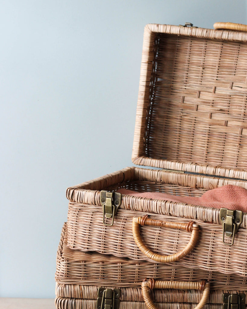 Two natural Rattan Toaty Trunks with leather straps and handles, stacked on top of each other against a blue-gray background.