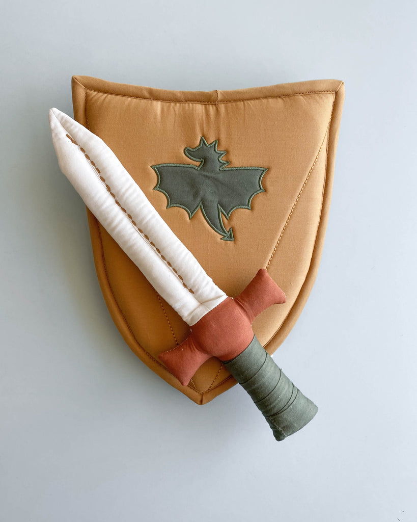 A fabric sword placed on top of a fabric shield, laying on a flat surface. 