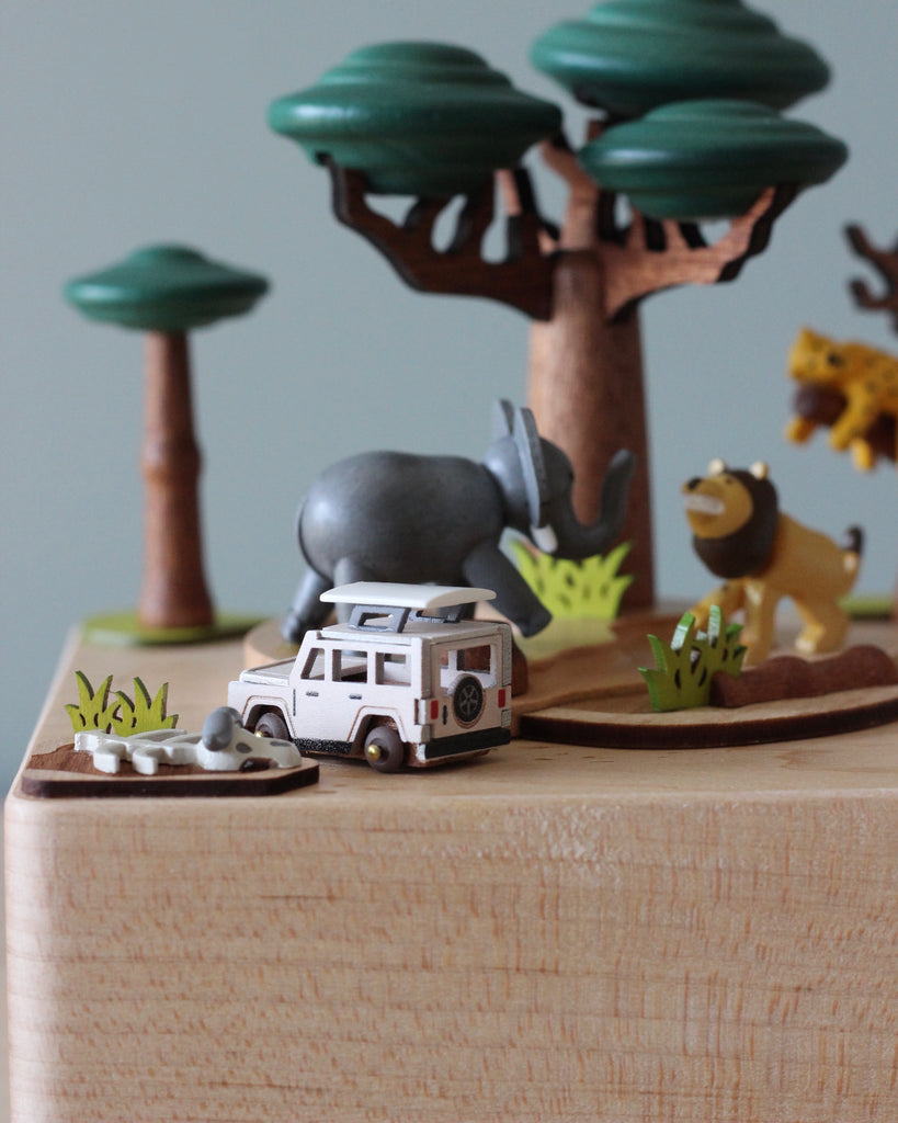 Wooden music box with a tree in the middle with African animals. A small wooden jeep going around the music box. 