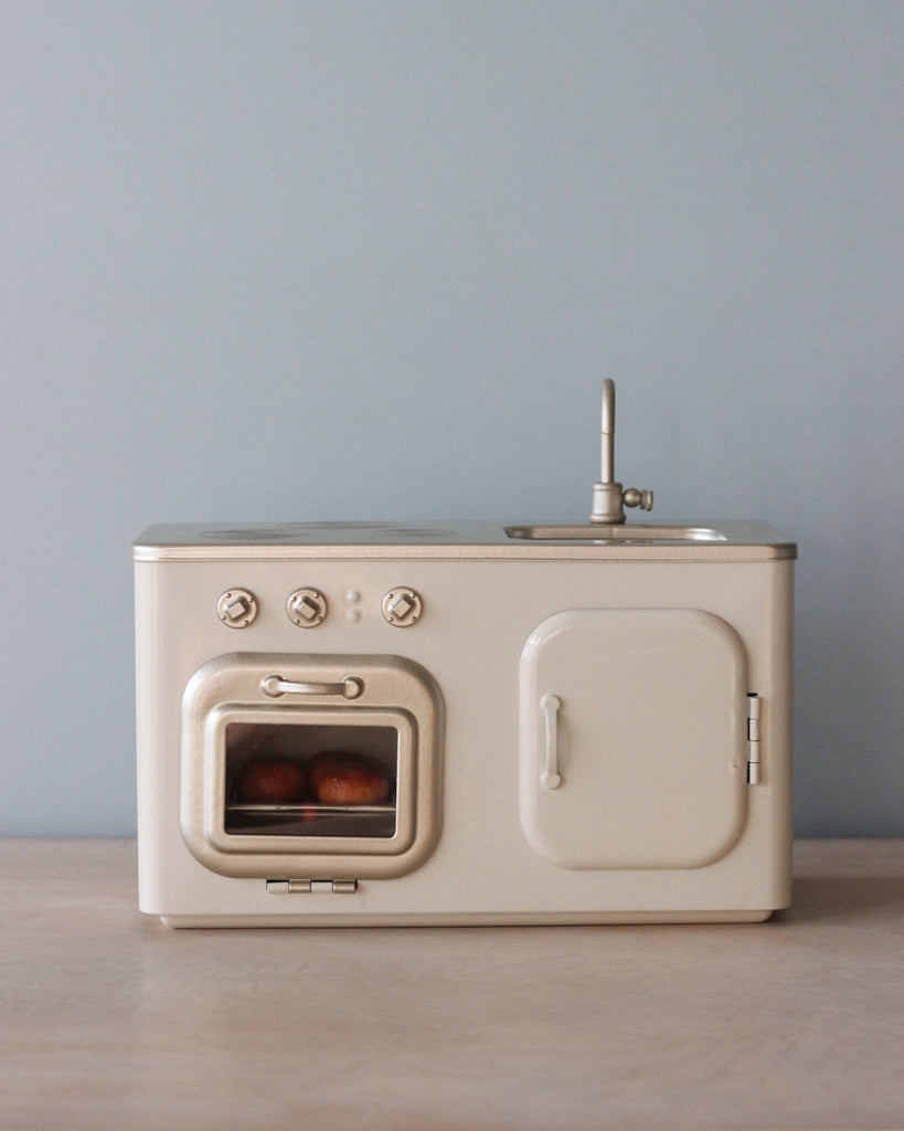 A Maileg Mini Kitchen with a window showing two small freshly baked buns inside, on a light blue background.