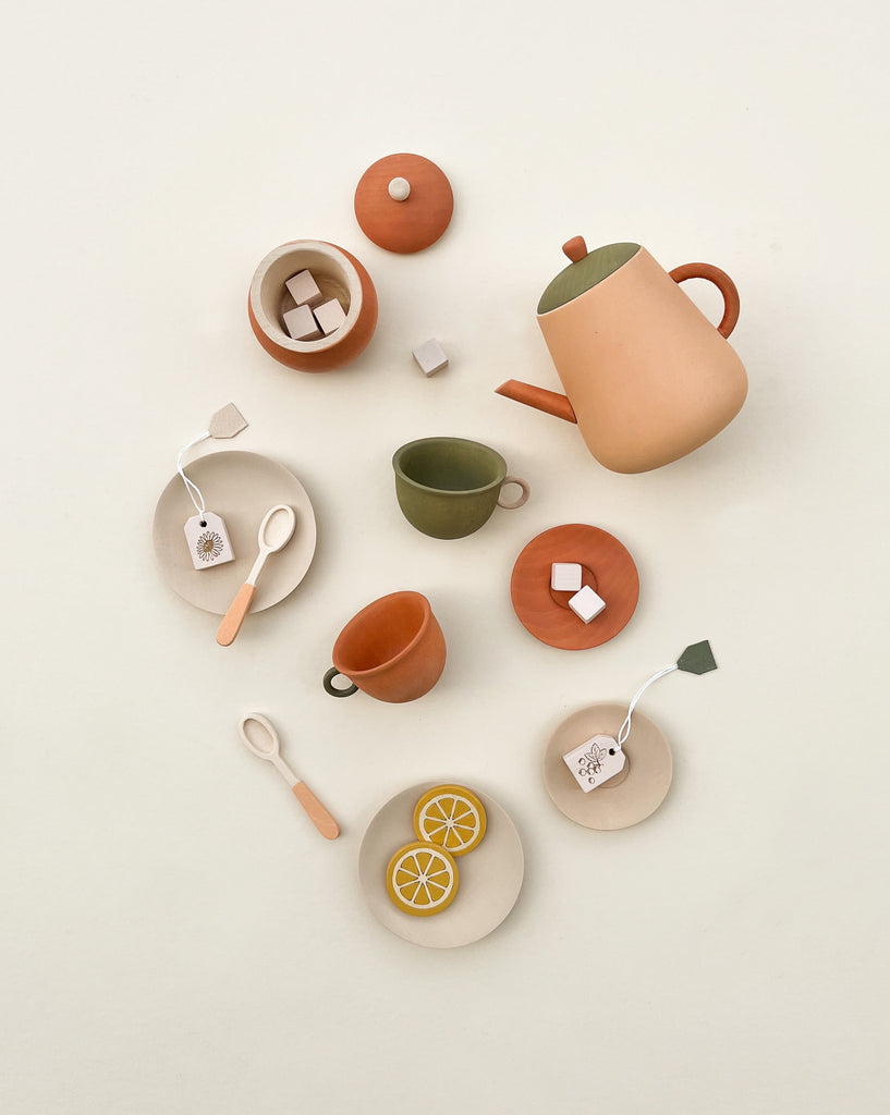 A neatly arranged overhead view of a Handmade Wooden Tea Set - Herbal and accessories, including a teapot, cups, sugar cubes, lemon slices, and tea bags on a soft beige background.