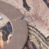 Close-up of a partially completed Londji - Dino Explorer Puzzle (350 pcs) featuring muted tones and an image of feathers. The puzzle's edge boasts a unique curved design and is prominently positioned in the foreground, with a small blue symbol visible on one of the pieces—an educational toy perfect for curious minds.