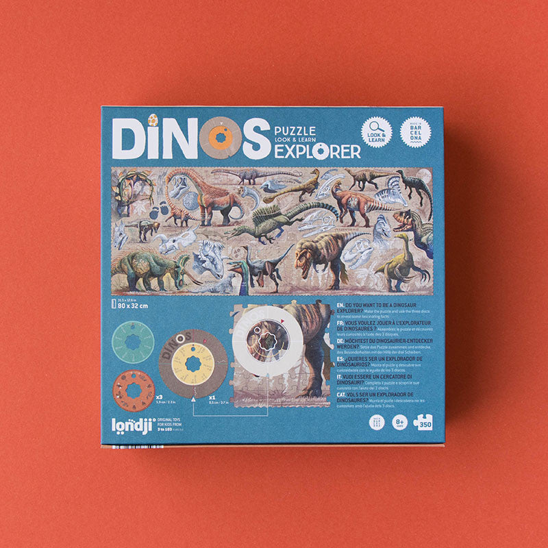 A box containing the "Londji - Dino Explorer Puzzle (350 pcs)" is shown against a red background. The blue box features illustrations of various dinosaurs and a kaleidoscope. This educational toy puzzle, measuring 80x32 cm with 350 pieces, proudly displays the Londji brand name at the bottom.