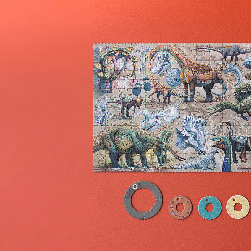 The Londji - Dino Explorer Puzzle (350 pcs), once completed, showcases various dinosaur species against an orange background. Beneath the puzzle, four circular washers of different sizes and colors are neatly arranged in a row. This educational toy effectively merges entertainment with learning through sustainable play.