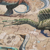 A close-up of the Londji - Dino Explorer Puzzle (350 pcs) depicting various dinosaur species. The pieces are interlocked, showcasing several dinosaurs with distinct colors and features. One prominent dinosaur has a green, scaly body and is mid-growl with its sharp teeth exposed. This educational toy is both fun and engaging.