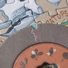 A close-up of interconnected jigsaw puzzle pieces from the Londji Dino Explorer Puzzle (350 pcs) depicting nature-themed illustrations. The pieces fit together, showcasing various shapes, colors, and textures that include fish, leaves, and a partially visible word "PTOPS." This educational toy focuses sharply on the puzzle's edge.