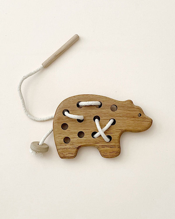 A wooden lacing toy shaped like a bear, designed for developing hand-eye coordination, with holes and a white lace threaded through some of them, against a pale background.