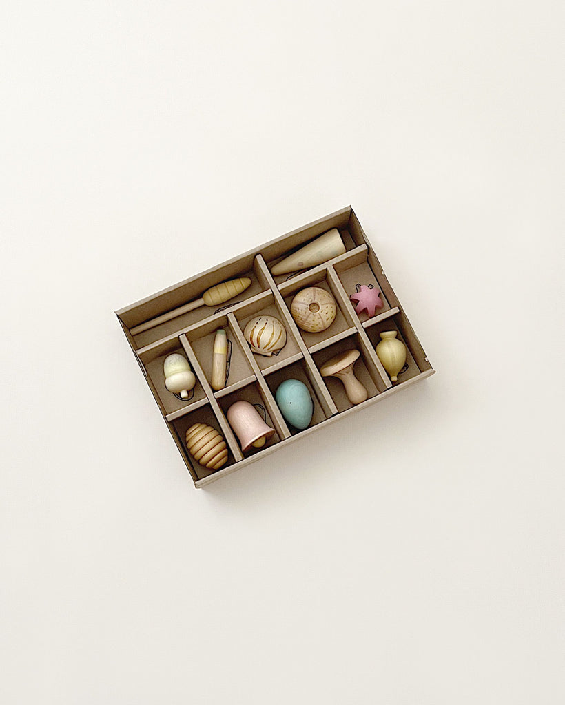 A wooden organizer box containing a variety of small items including seashells, Grapat Wonders Play Set, and pebbles, all neatly arranged in separate compartments against a light background.