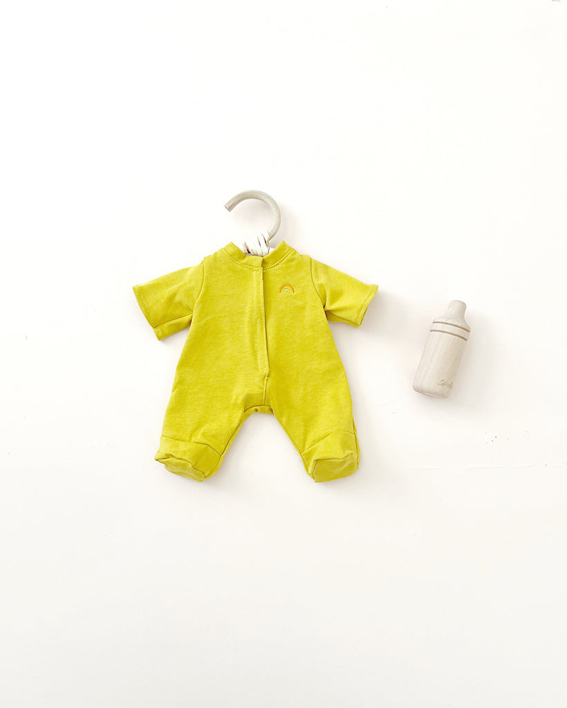 A Olli Ella | Dinkum Doll Extra Clothing onesie hanging on a white hanger accompanied by a small baby bottle, all against a plain white background.