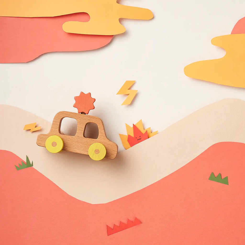 A creative paper art scene featuring My Little Car toy car traveling through a layered landscape of soft pink and orange hills, with paper cut-outs of clouds, lightning bolts, and small green shrubs.