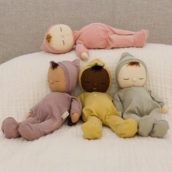 Four soft dolls with different skin tones in pajamas under a gauze blanket. 