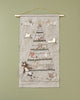 A Coral & Tusk Embroidered Advent Calendar fabric wall hanging featuring a countdown to Christmas design with embroidered animals, stars, and small gifts, hung on a wooden rod against a green wall.