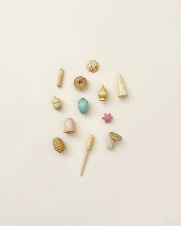 Assorted small, pastel-colored Grapat Wonders Play Set from sustainable forests, including spinning tops, blocks, and shapes, arranged neatly on a light background.