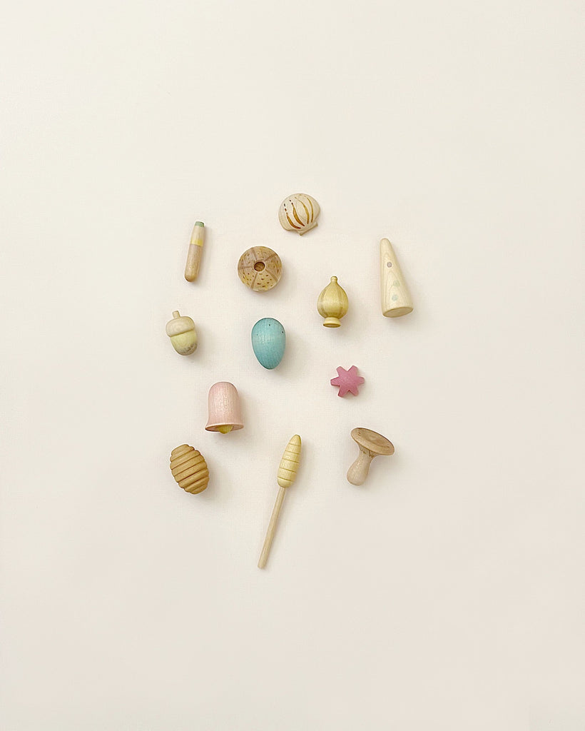 Assorted small, pastel-colored Grapat Wonders Play Set from sustainable forests, including spinning tops, blocks, and shapes, arranged neatly on a light background.