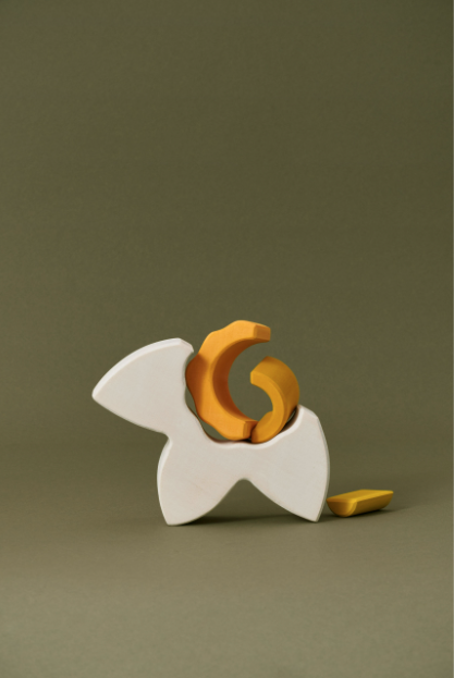 Abstract wooden sculpture featuring interlocking white and gold pieces from Raduga Grez Arch Stacker - Narcissus Flower, displayed against a green background.