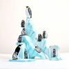 Handmade Wooden Penguin Set creates a playful, Waldorf-inspired scene. One larger penguin stands atop the highest iceberg, while seven smaller penguins are scattered on various ledges. The background is bright and minimalistic, highlighting the vivid blue and white of the handmade Antarctica scene painted with non-toxic paints.